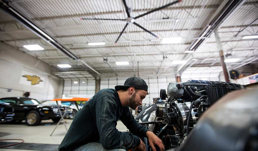 Mechanic working on a car under an HVLS fan.